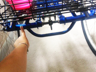 finger pointing to the left back axle of an adult trike where a trike adaptor attaches